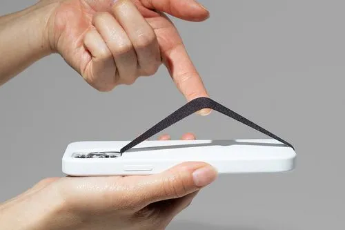 Close-up of a hand demonstrating a minimalist elastic phone grip on a white smartphone case, providing a secure and ergonomic hold.