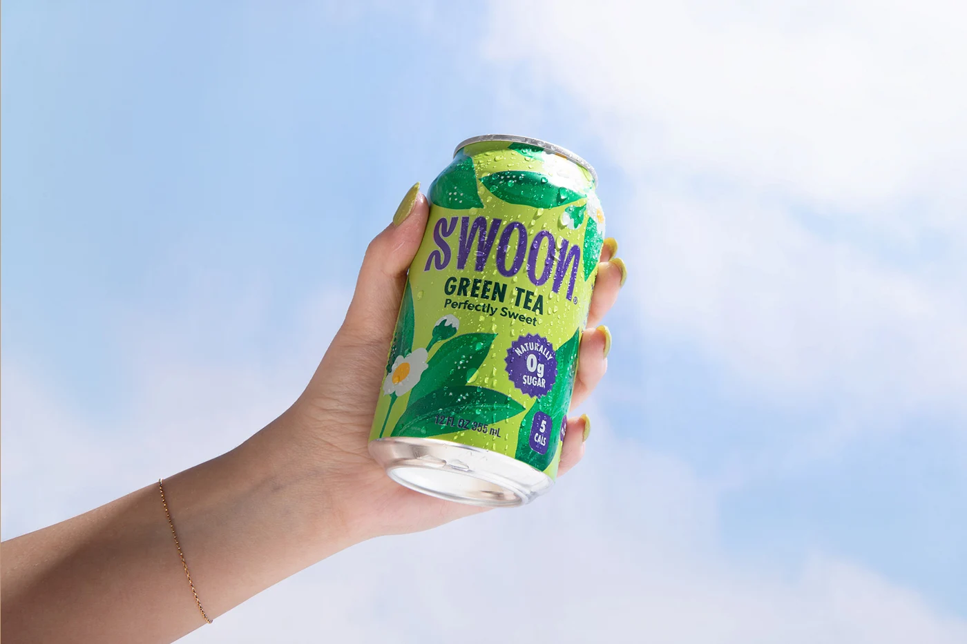 a hand holding a Swoon green tea can in front of a blue sky