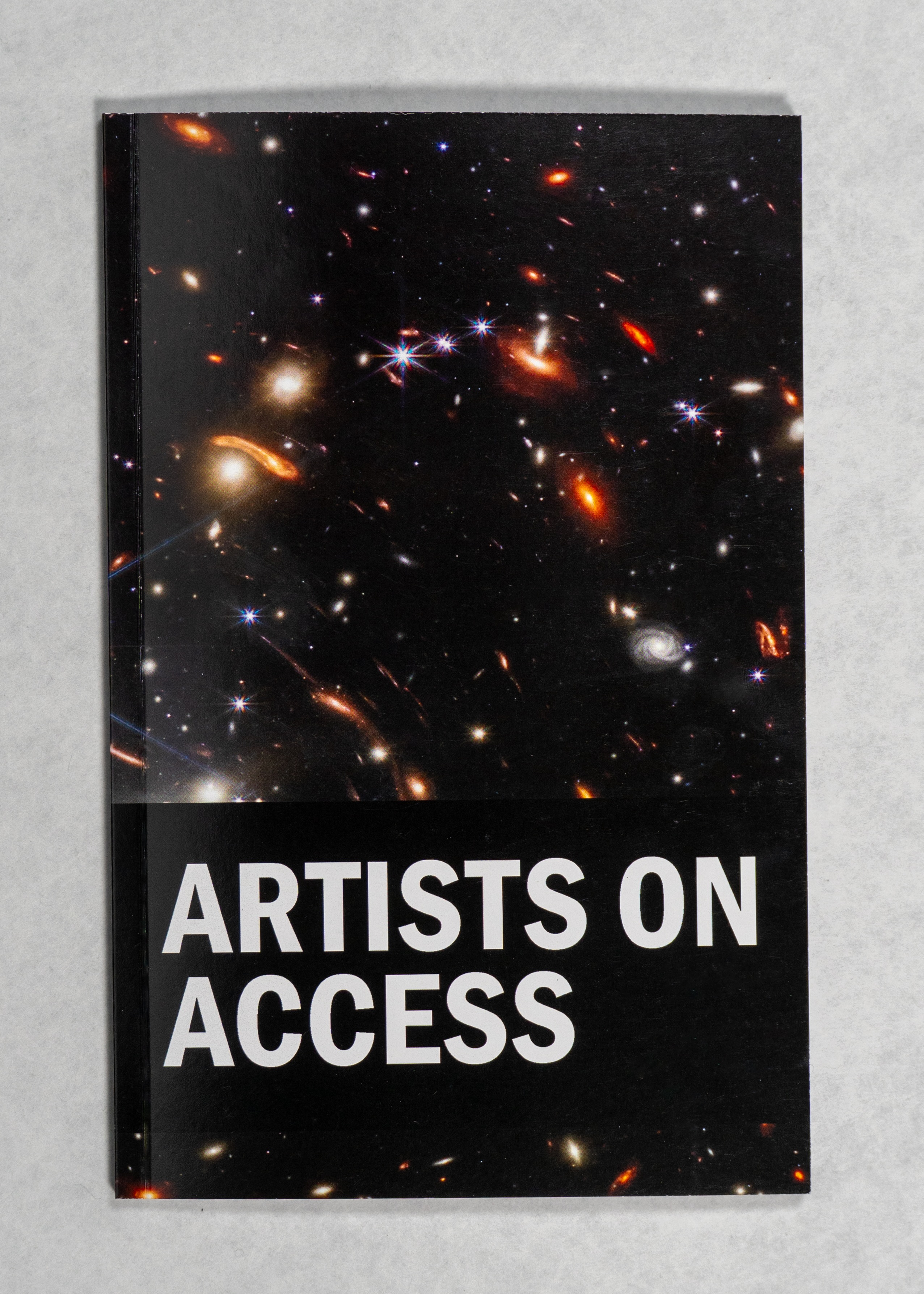 Artists on Access  A black book on a white background. The bottom half reads ARTIST ON ACCESS in white text, and the top half features an image of a galaxy, with a colourful arrangement of yellow, red, white and blue stars and galaxies.