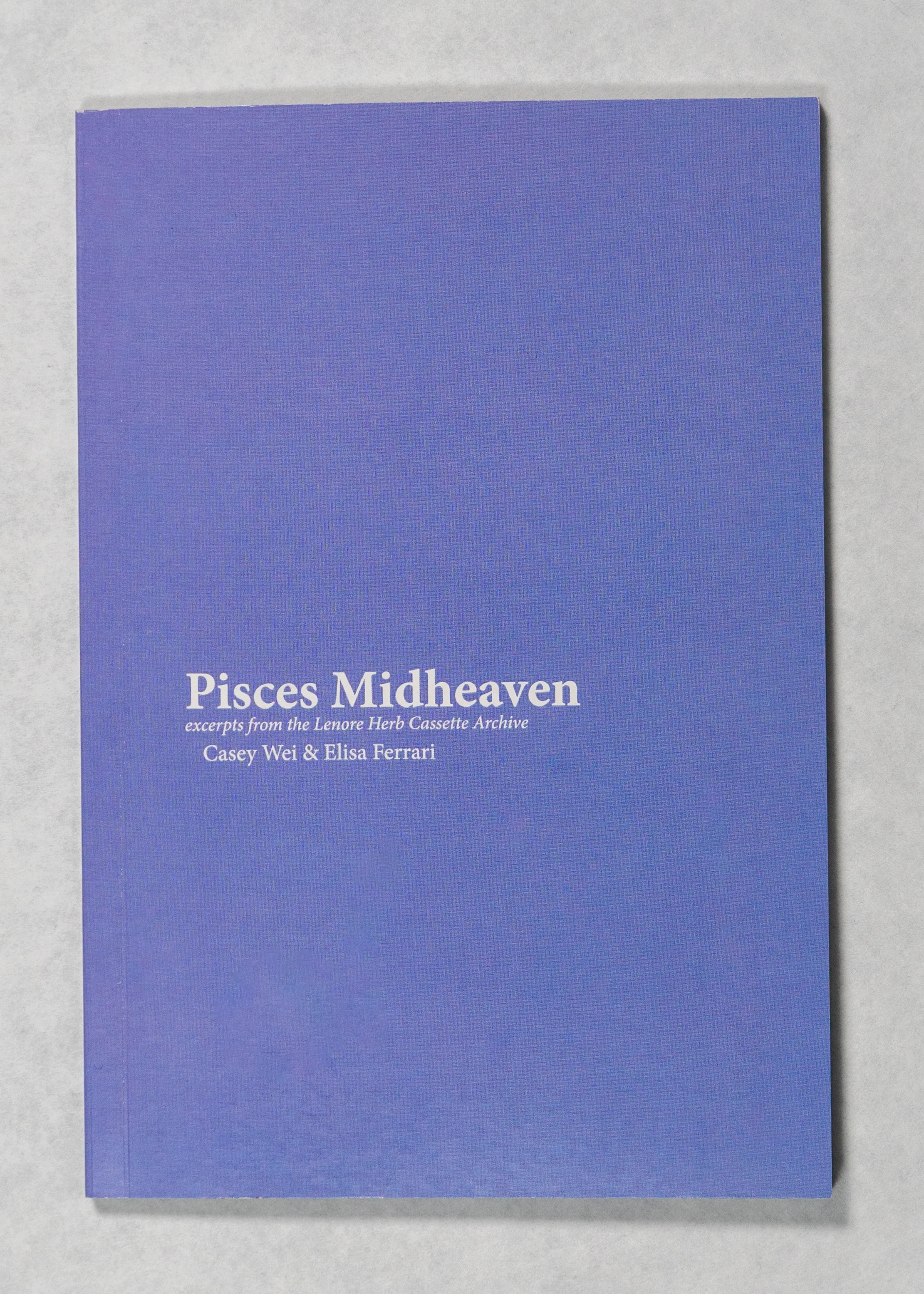 A blue book with white text reading “Pisces Midheaven - excerpts from the Lenore Herb Cassette Archive - Casey Wei and Elisa Ferrari” on a white background. 