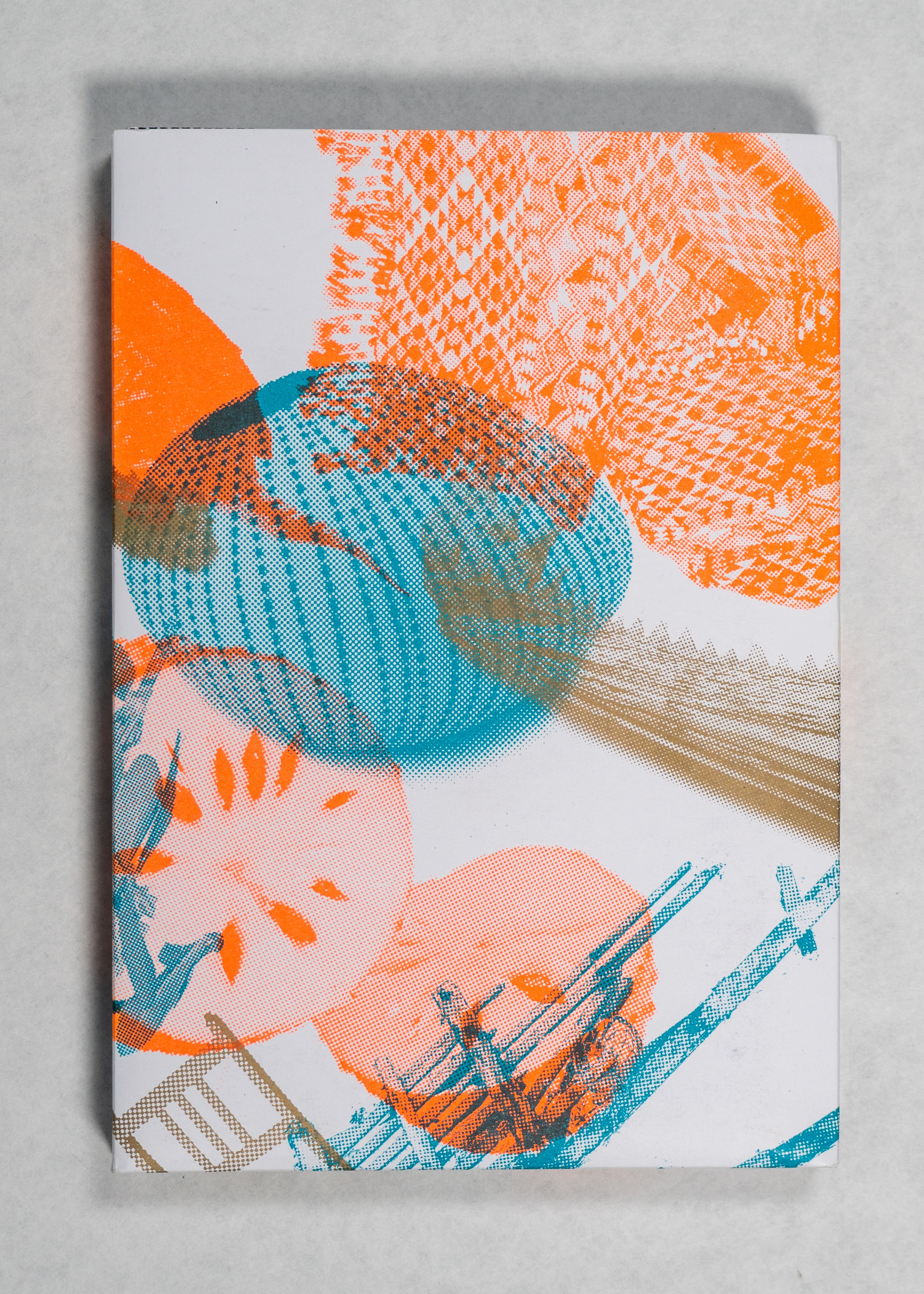 A white background featuring a rectangular collection of notes; the cover of which is white and adorned with overlapping, semi-transparent images of cloth, fruits, and chairs, varying in colour from blue to orange to grey. 