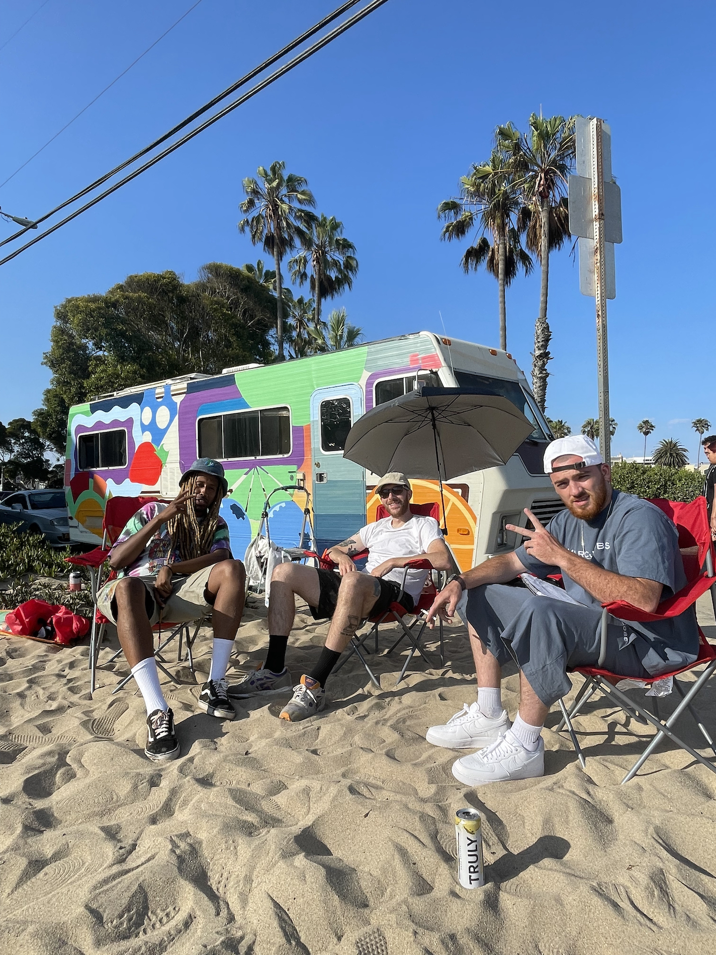 Three people sitting on sand in front of Truly Hard Seltzer hand painted Winnebago