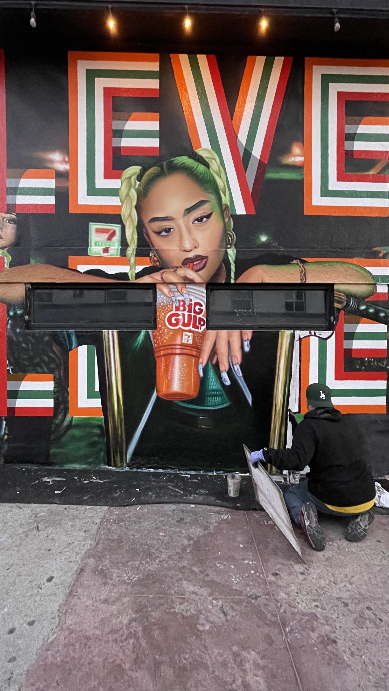 Closeup of 7-Eleven hand painted mural in Venice CA showing Eleven lettering in red green and orange with photorealistic portrait
