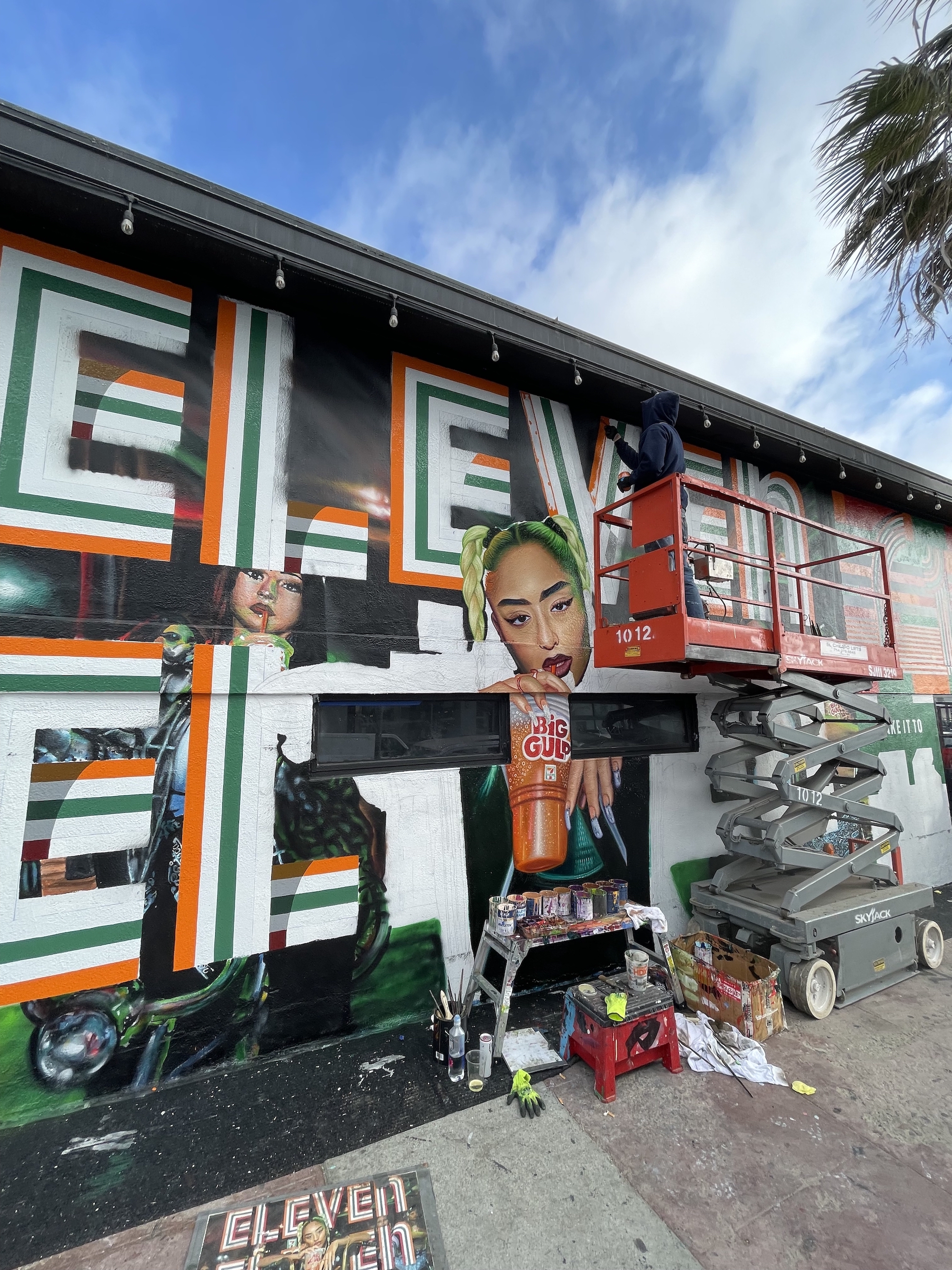 Hoist Media artist on scissor lift adding hand-painted detail to 7-Eleven mural in Venice CA