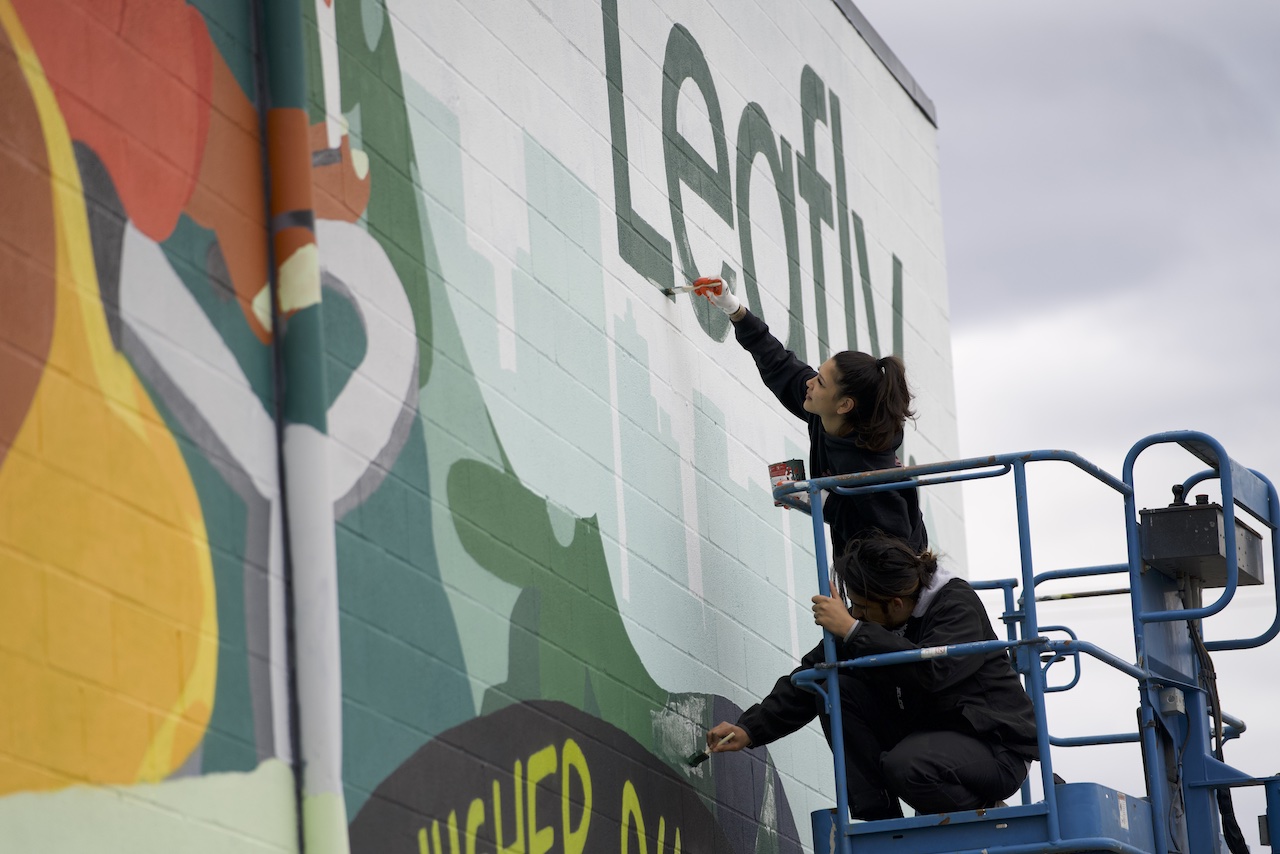 Hoist Media artists on scissor lift hand-painting Leafly logo and lettering on building exterior in Portland