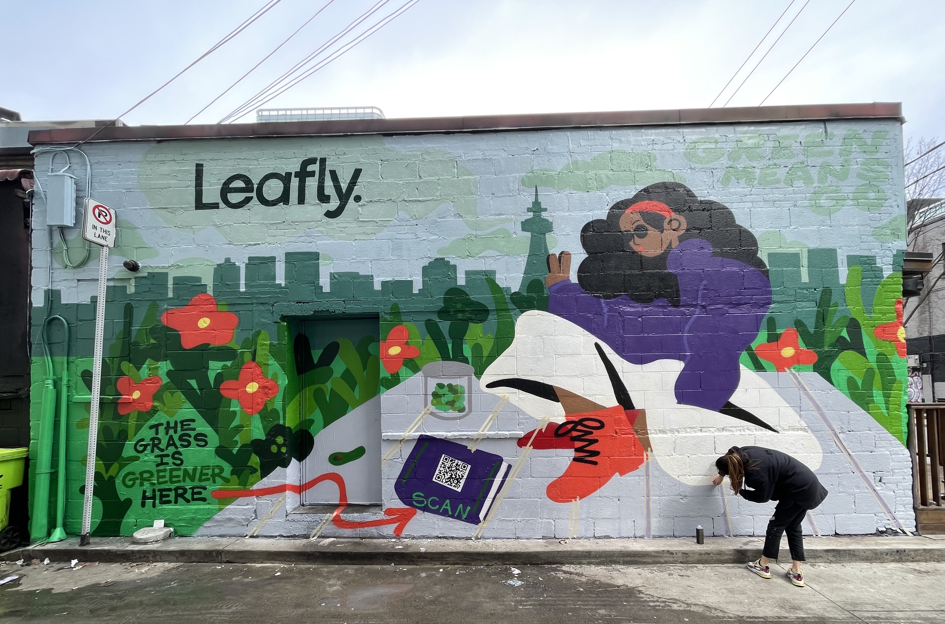 Hoist Media artist finishing Leafly cannabis mural with illustrated figure and QR code on building exterior in Toronto