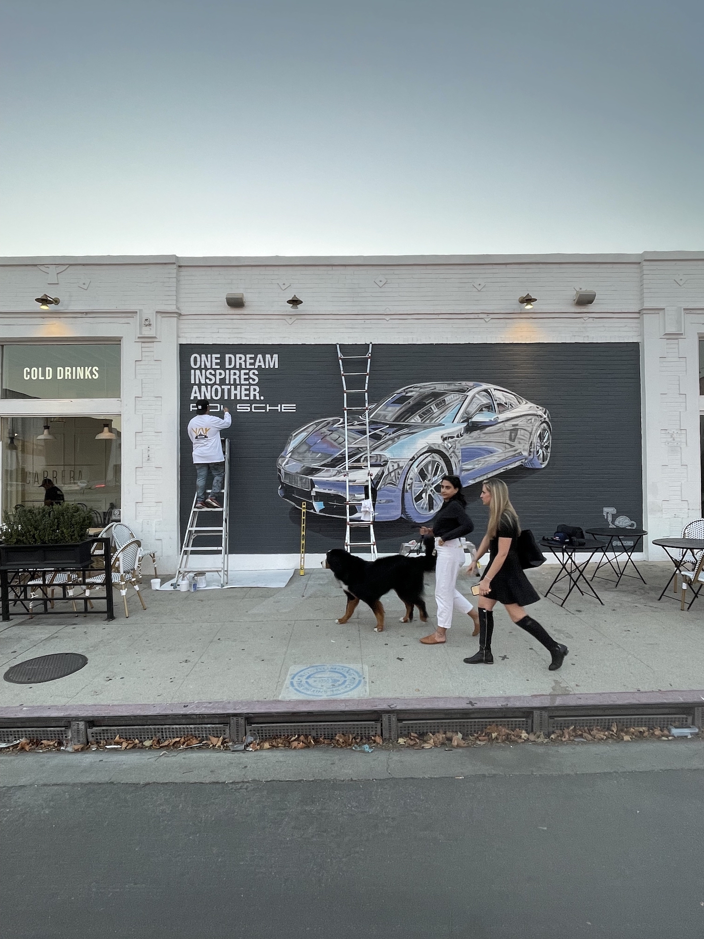 Hoist Media artist on ladder finishing photorealistic Porsche Taycan hand painted mural on West Hollywood brick wall