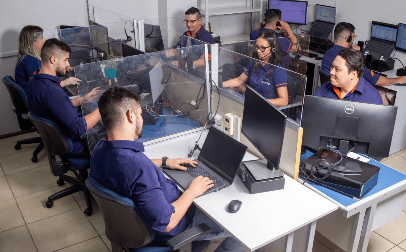Equipe de escritório trabalhando em computadores com divisórias de acrílico para proteção.