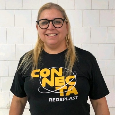 Mulher sorridente de óculos e camiseta preta com texto Connecta Redeplast em azulejos brancos.