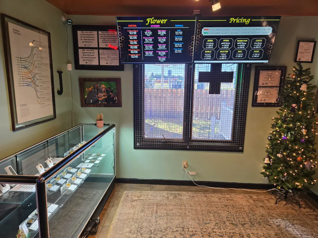 Photo of an inside perspective of the Montana Janes Bozeman dispensary that includes a product display counter and overhead cannabis product menu, with a decorated Christmas tree in the corner