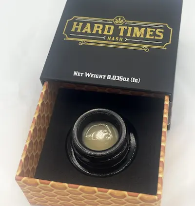 Hard Times Hash rosin in small black container inside a black and honeycomb-patterned box.