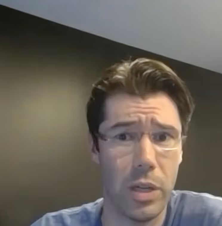 A man wearing glasses and a blue shirt is engaged in conversation.