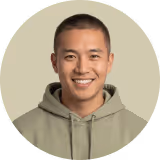 Smiling man wearing a light brown hoodie against a beige background.