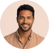 Smiling man with short curly black hair wearing a brown shirt against a beige background.