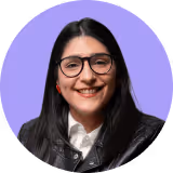 Smiling woman with black hair, glasses, and a leather jacket on a purple background.