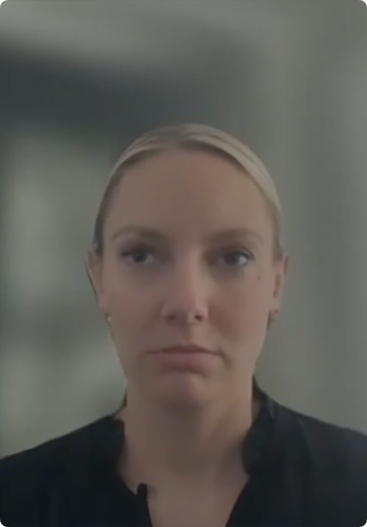Portrait of a woman with blonde hair pulled back, wearing a black top, against a blurred background.