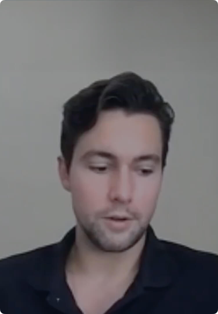 Young man with dark hair and a short beard wearing a black shirt, looking downwards.