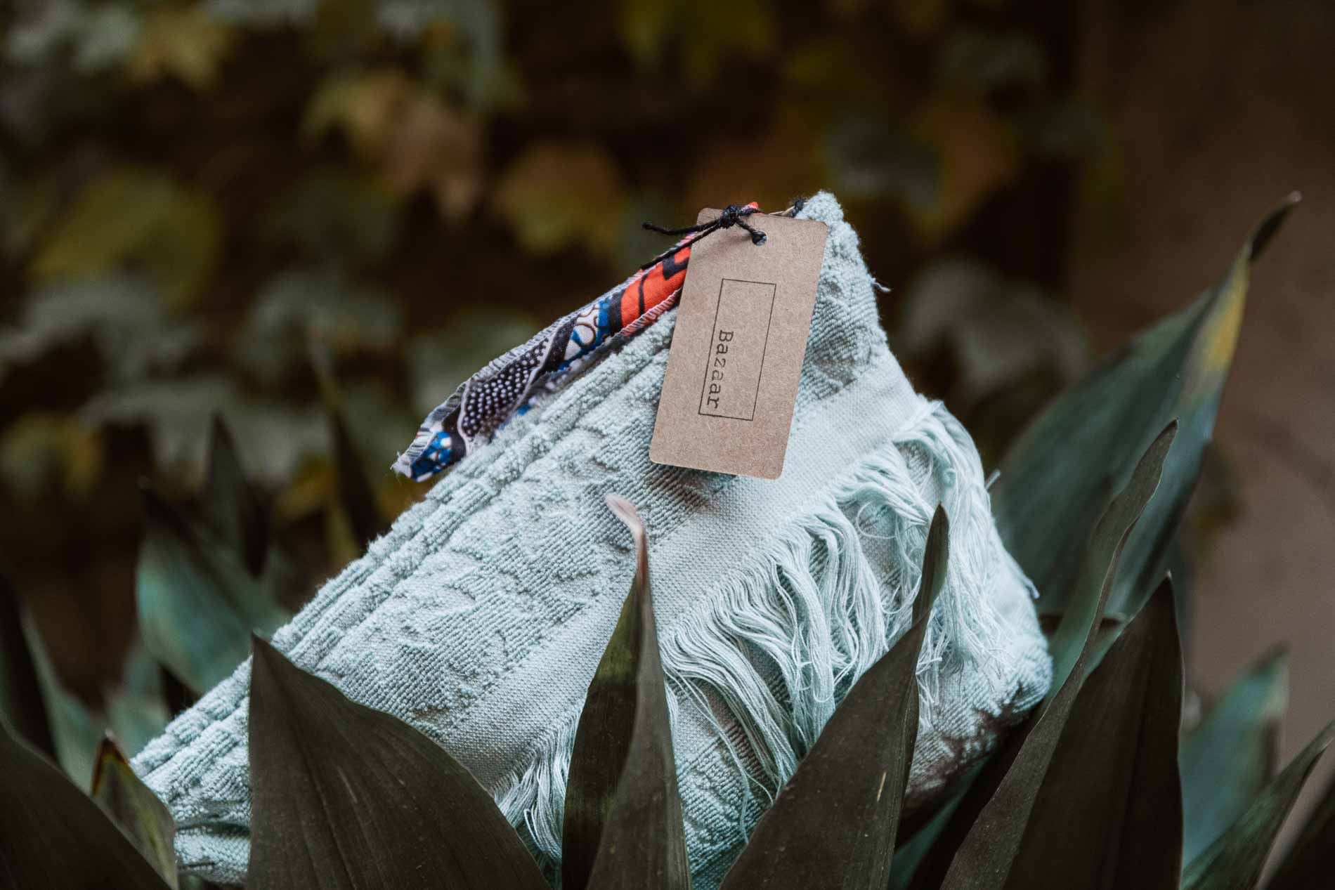 Bolso de mano de toalla en color azul claro sobre base de planta verde de hojas grandes