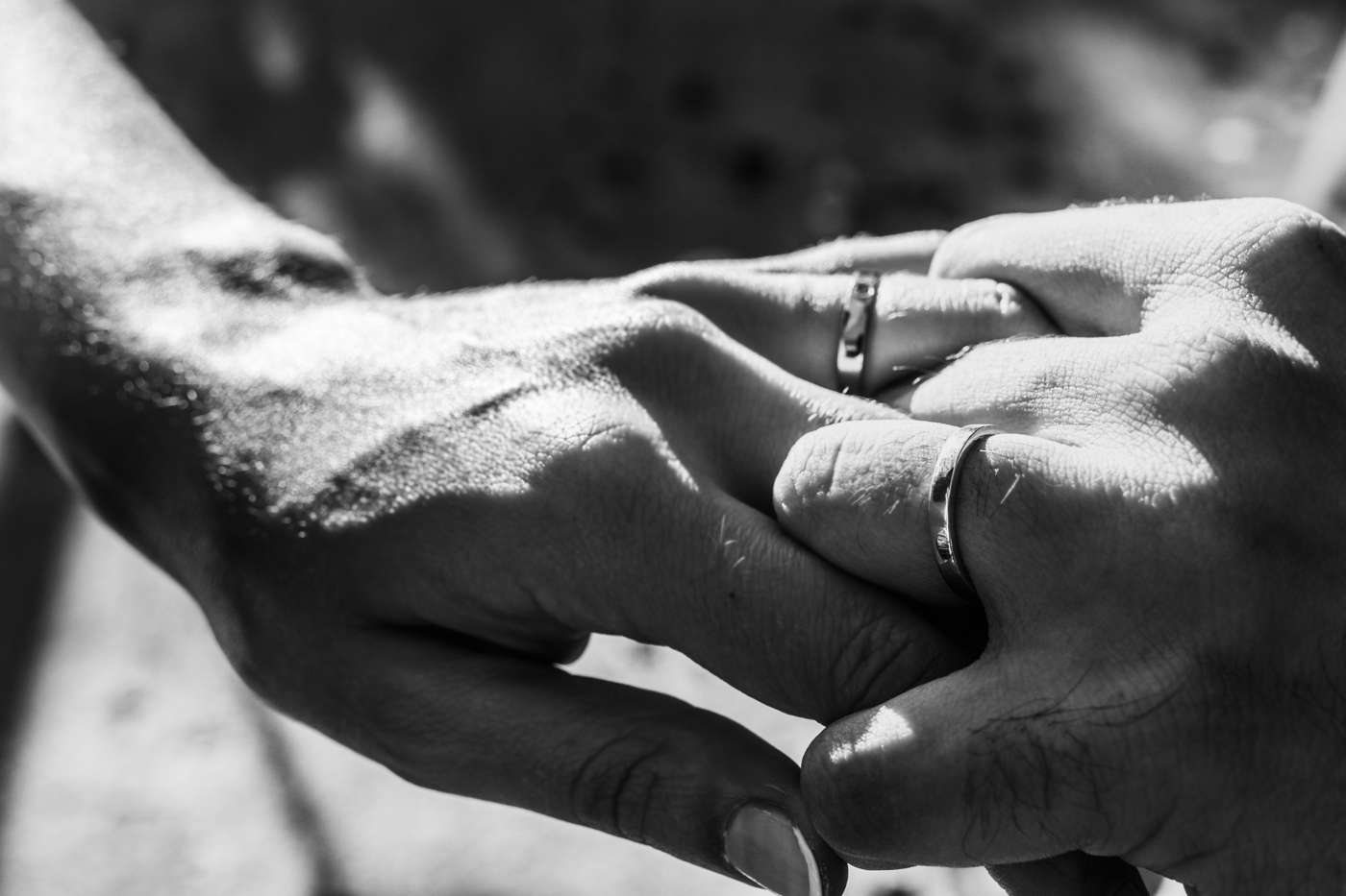 Primer plano en blanco y negro de dos manos entrelazadas, ambas con anillos de boda.