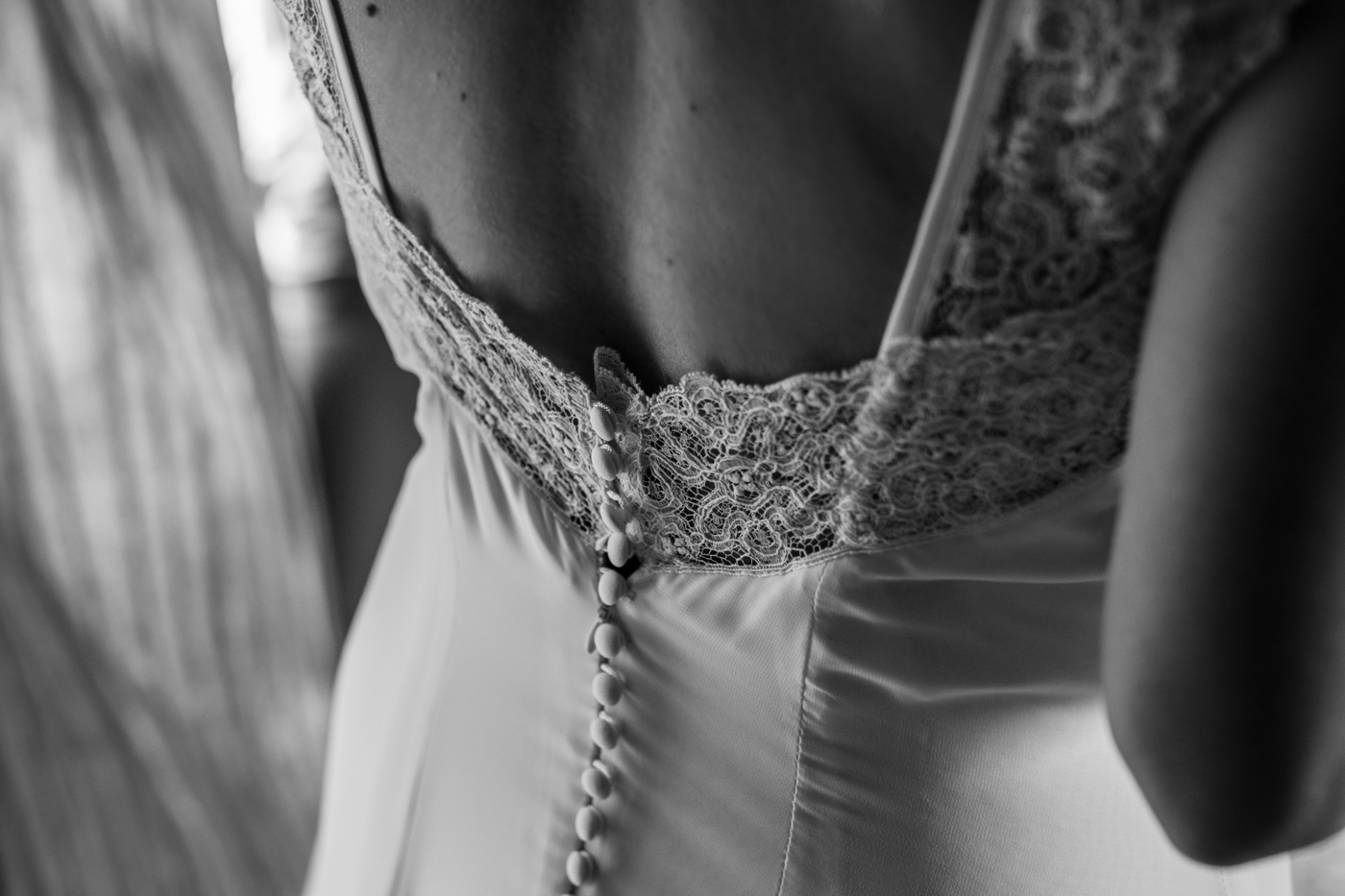 Primer plano de la espalda de una novia mostrando detalles de encaje y botones en un vestido de boda.