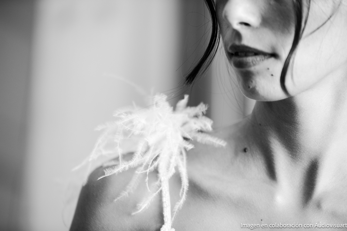 Primer plano en blanco y negro del hombro y la parte inferior del rostro de una mujer, mostrando un tejido de textura delicada sobre su hombro y mechones de cabello sueltos.