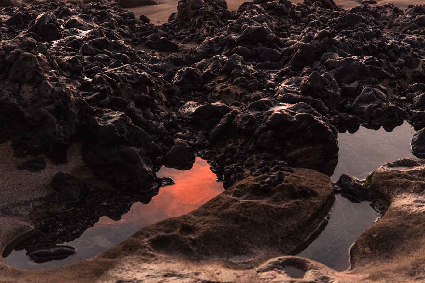 Charcas de marea rocosas que reflejan los tonos naranjas de un atardecer.