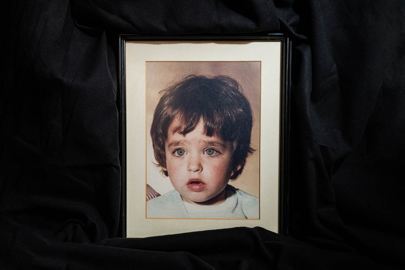 Retrato enmarcado de una niña pequeña con pelo castaño corto y ojos verdes, vestido con una camiseta de color claro.