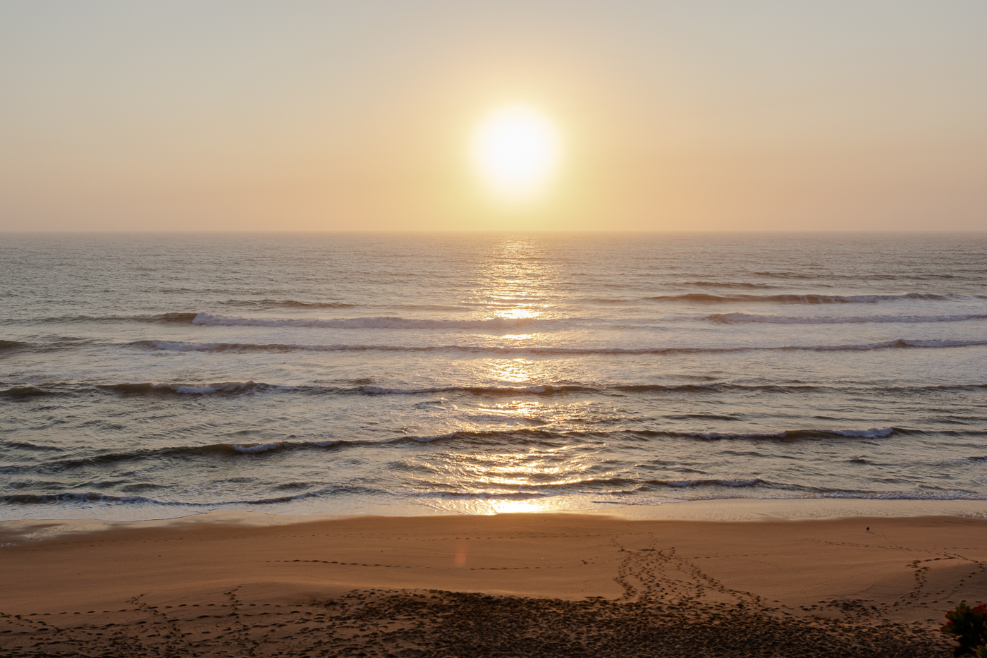 Atardecer sobre las olas del océano, con una playa de arena en primer plano.