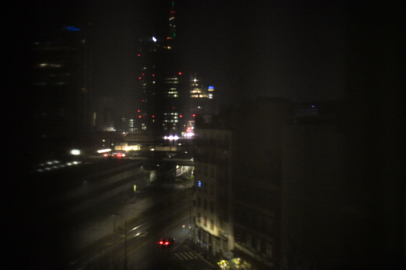 Paisaje urbano nocturno con rascacielos iluminados y farolas, visto desde arriba.