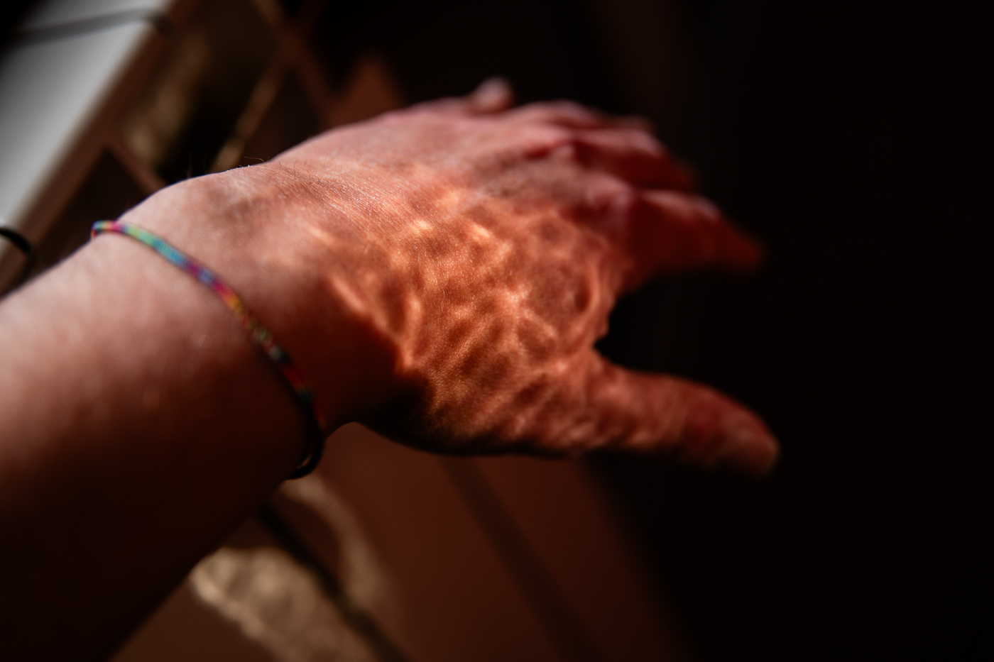 Primer plano de una mano con una pulsera tejida de colores, con reflejos de luz sobre la piel.