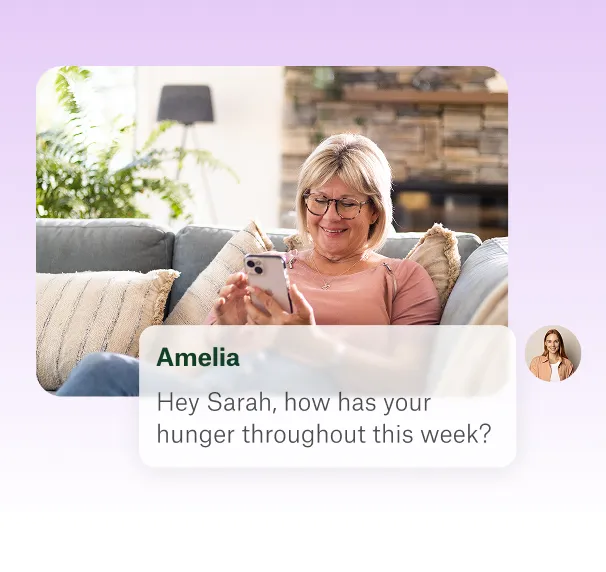 Smiling woman sitting on a couch looking at her smartphone with a chat message from Amelia asking how Sarah's hunger has been throughout the week.