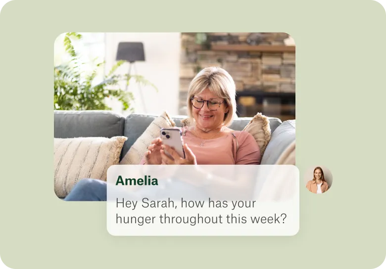 Smiling woman sitting on a couch looking at her phone with a chat message on screen asking about her hunger this week.