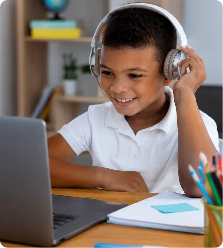 Young boy with headphones smiling while looking at a laptop during virtual learning.