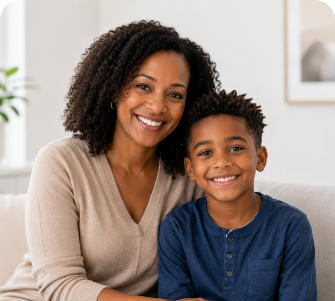 Smiling woman with curly hair sitting next to a happy young boy in a blue shirt on a couch.