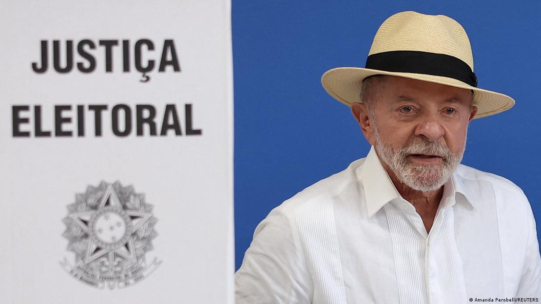 Lula da Silva, con sombrero panamá y camisa blanca, junto a un biombo de la Justicia Electoral al votar en Brasil