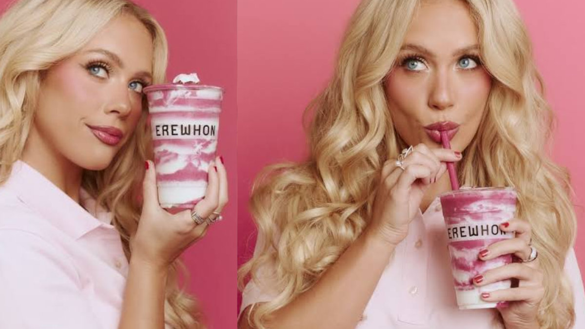 Mujer rubia sosteniendo y tomando un smoothie rosa en un vaso de Erewhon, fondo rosado