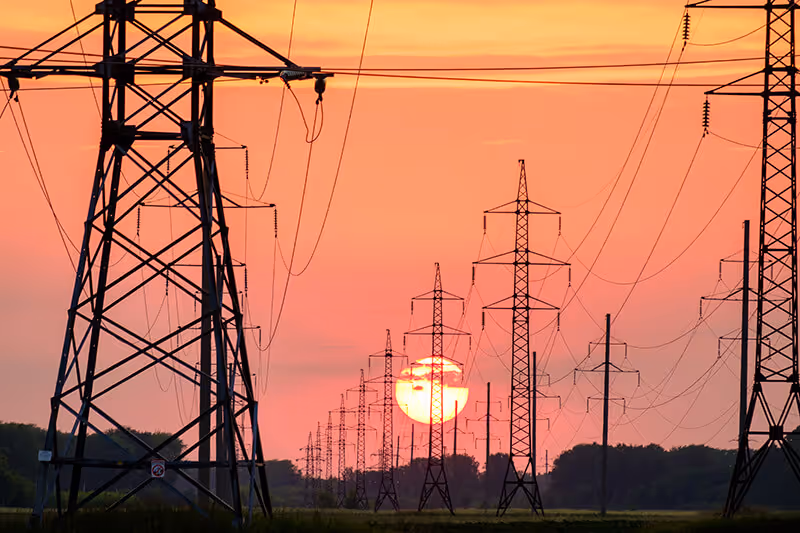 Sun setting in the background with silhouettes of powerlines in the foreground