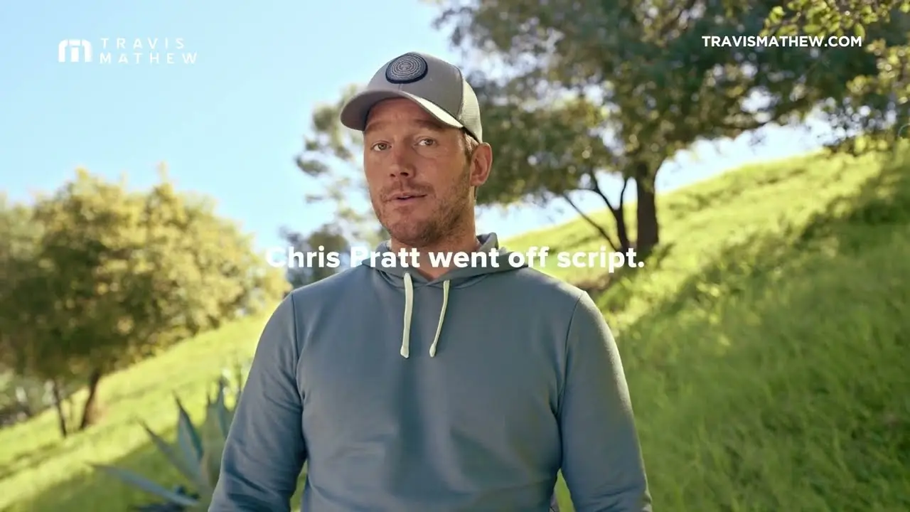 Man in a light blue hoodie and baseball cap standing outdoors with green trees and grass in the background, with a caption stating "Chris Pratt went off script."