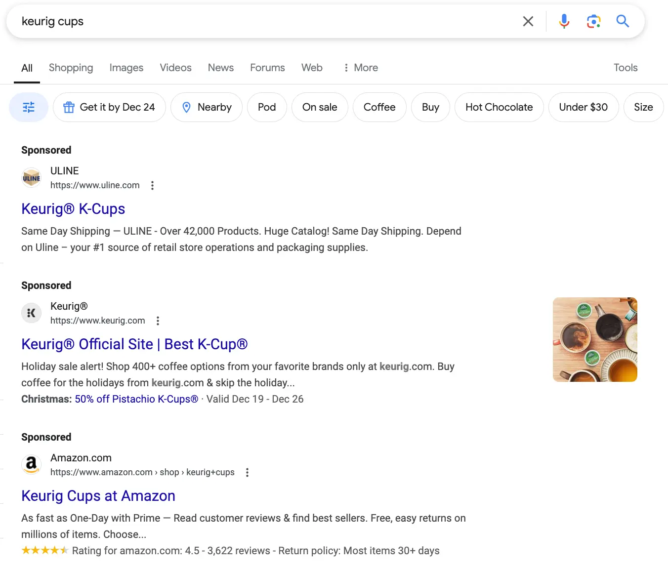 Screenshot of a Google search results page for "keurig cups" showing various advertisements for Keurig K-Cups including links to purchase options from Keurig's official site and Amazon, and a search bar with filter options like 'Nearby', 'On sale', and 'Under $30'.