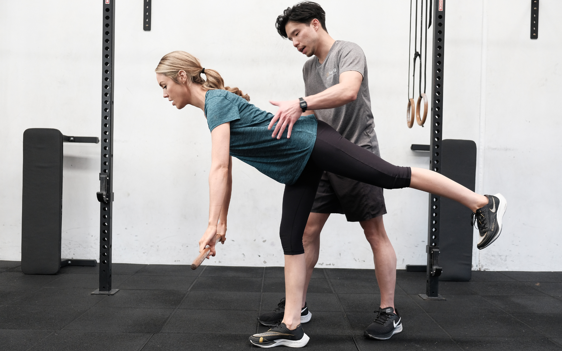 En fysioterapeut hjälper en patient att utföra en balansövning på ett ben i ett gym.