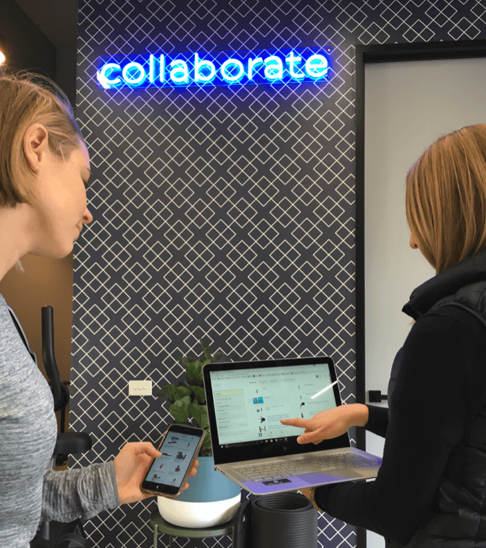 Two staff members at Upwell Health Collective reviewing patient information on a tablet near the neon 'collaborate' sign.