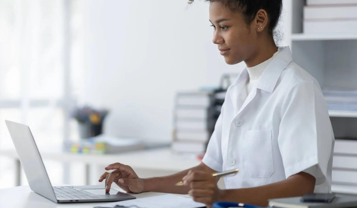 A healthcare professional in a white coat using a laptop at a desk, representing online continuing education for practitioners.