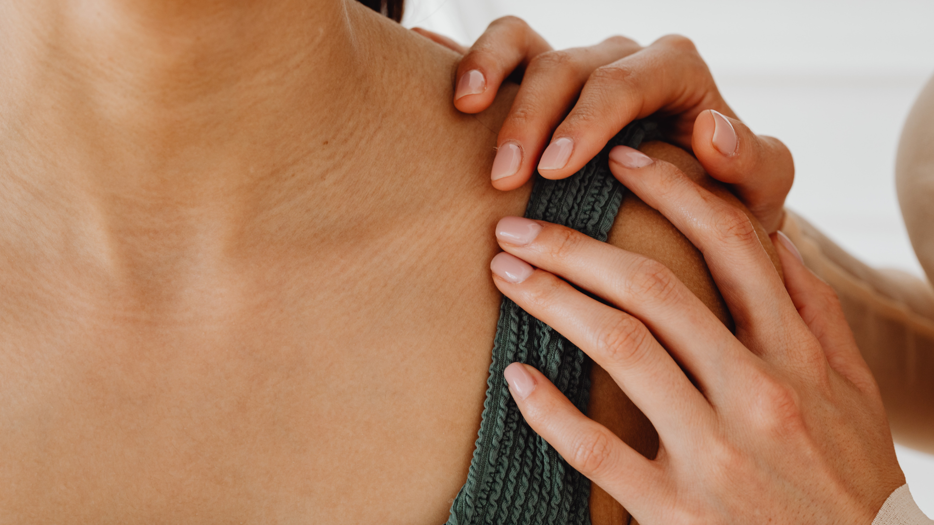 Close-up of a therapist's hands applying manual therapy to a patient's upper trapezius and shoulder area.