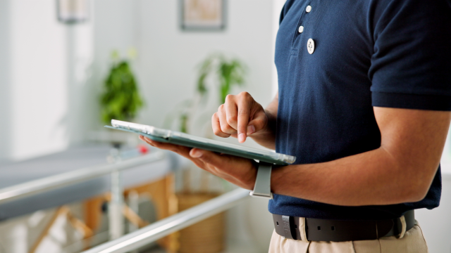 Ein Mann in einem marineblauen Poloshirt, der in einem hellen Büro steht und ein Tablet benutzt