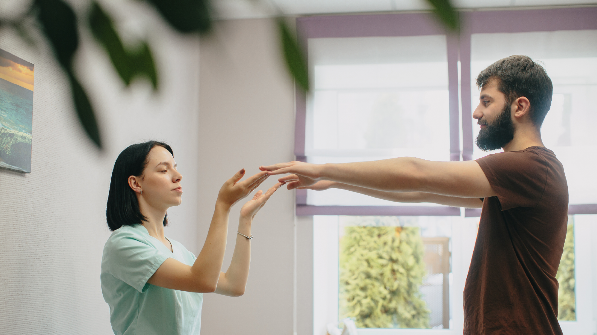 Physiotherapist guiding a man through a balance and awareness exercise with outstretched hands in a treatment room