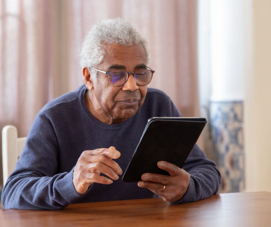 Older man wearing glasses using a tablet at a dining table at home