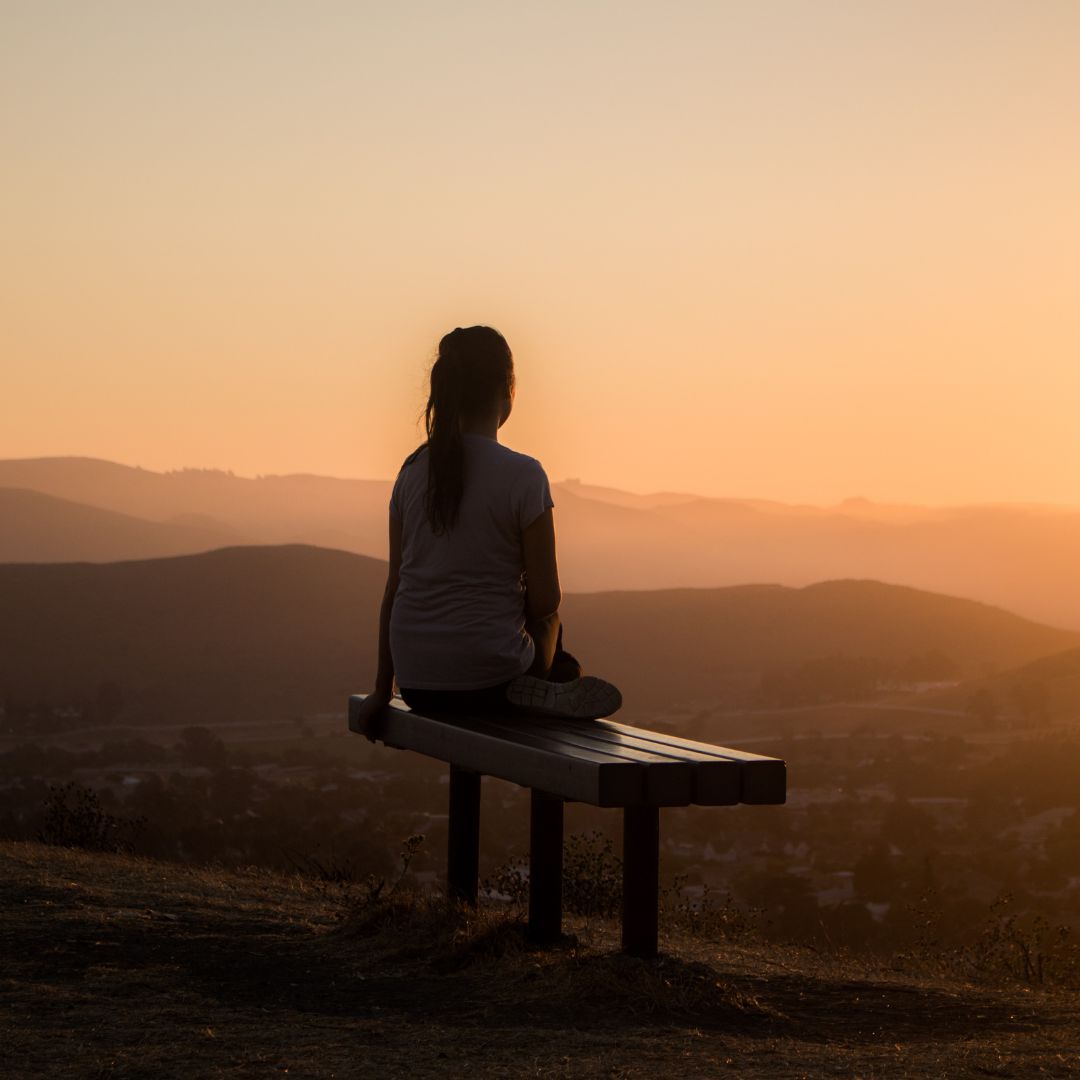 Person sitting alone on a bench overlooking hills at sunset