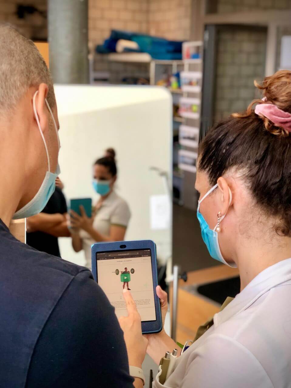 Two clinicians wearing face masks looking at an exercise video on a tablet in a clinic