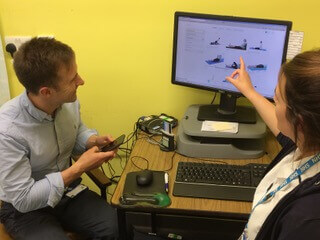 Two clinicians at a desk looking at a monitor, one pointing at the screen during a session.
