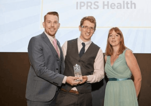 Three people on stage holding a glass star award beneath an IPRS Health screen